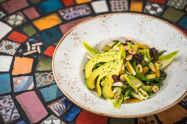Fresh salad with with avocado and nuts in plate on background of oriental pattern