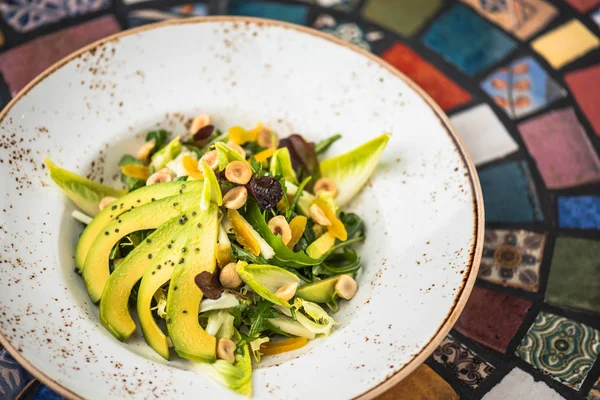 Fresh salad with with avocado and nuts in plate on background of oriental pattern