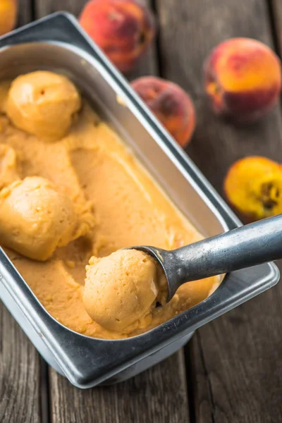 Peach ice cream in container with spoon on wooden table