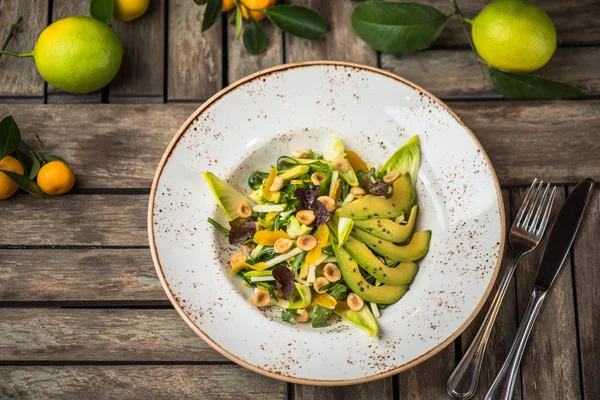 Fresh salad with avocado and nuts in plate on wooden table