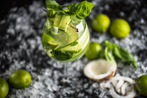 Cocktail with basil, lime and coconut in glass on dark background with ice