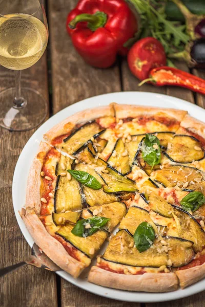 Baked vegetable pizza with aubergine and pine nuts on plate on wooden table