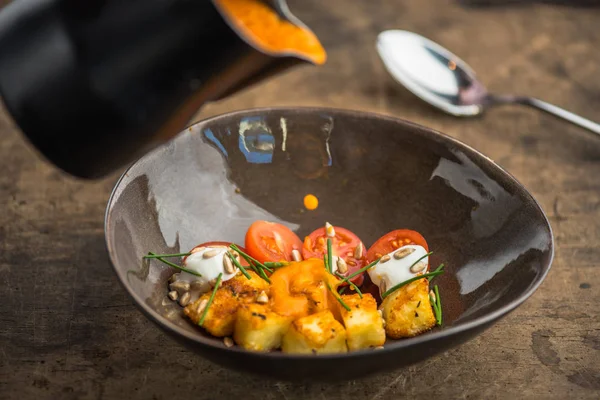 pouring vegetable soup with cheese in bowl from jug on wooden table