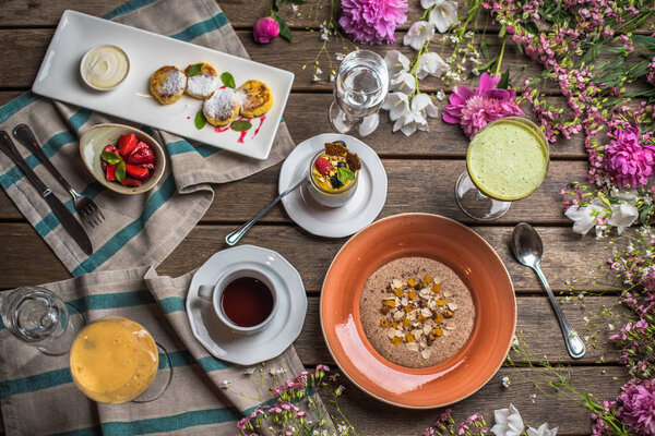 Breakfast wooden table with healthy dishes and flowers