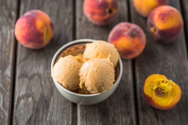 Peach ice cream balls in bowl on wooden table with fresh fruits