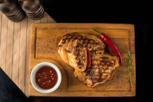 Grilled chicken served on wooden board with spicy sauce and chilli peppers