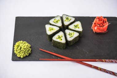 zencefil, wasabi ve gri arka plan üzerinde kayrak gemide yemek çubukları ile geleneksel üçgen suşi