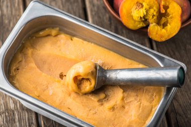 Ahşap masa kaşık ile kapsayıcısında şeftali dondurma