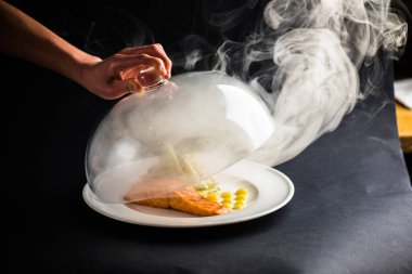 insan eli ile Somon parça ve siyah arka plan üzerine sebze salatası yemek üzerinden şeffaf kapak kaldırma 