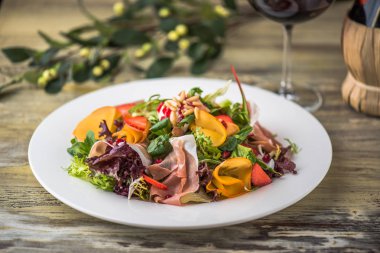Ahşap masa üzerinde beyaz tabakta sebze salatası jambon ile hizmet