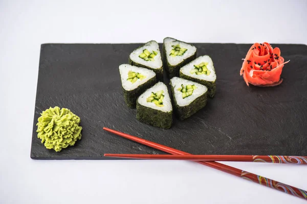 zencefil, wasabi ve gri arka plan üzerinde kayrak gemide yemek çubukları ile geleneksel üçgen suşi