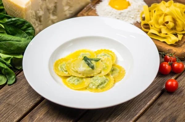 Traditional italian spinach ravioli served on white plate on wooden table with ingredients