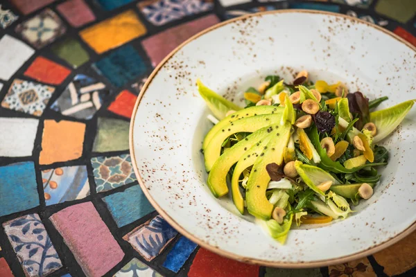 Fresh salad with with avocado and nuts in plate on background of oriental pattern