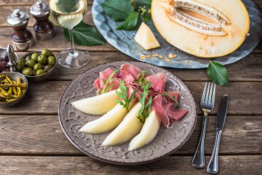 Aperatif plaka jambon ve kavun tabakta ahşap masa üzerinde beyaz şarap ile