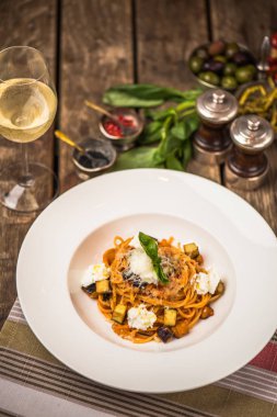 Ahşap masa üzerinde beyaz tabakta İtalyan makarna peyniri ve sebze ile servis