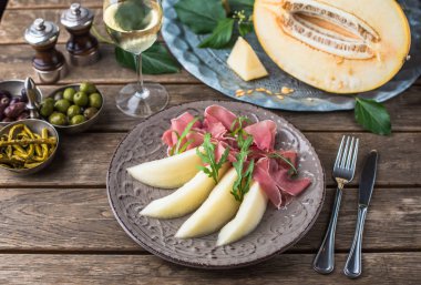 Aperatif plaka jambon ve kavun tabakta ahşap masa üzerinde beyaz şarap ile