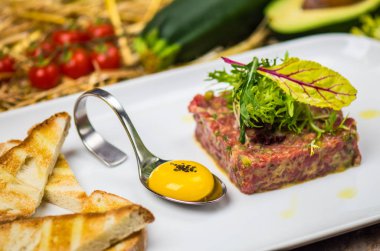 Taze tartar malzemeler ve arka plan üzerinde saman ile çiğ yumurta sarısı ve ekmek parçaları ile beyaz tabakta servis