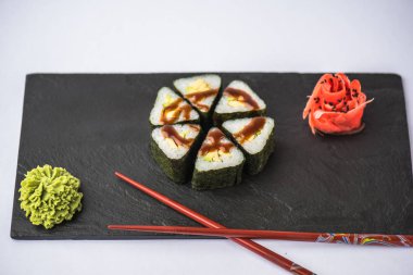 zencefil, wasabi ve gri arka plan üzerinde kayrak gemide yemek çubukları ile lezzetli üçgen suşi