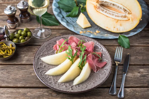Aperatif plaka jambon ve kavun tabakta ahşap masa üzerinde beyaz şarap ile