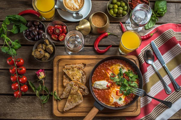 shakshuka, zeytin, biber, domates, ekmek, meyve suyu ve kahve rustik ahşap tablo ile kahvaltı