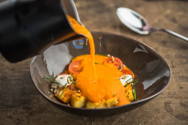 pouring vegetable soup with cheese in bowl from jug on wooden table