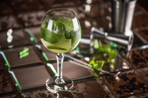 Cocktail with mint leaves and ice in glass on brown tiled background