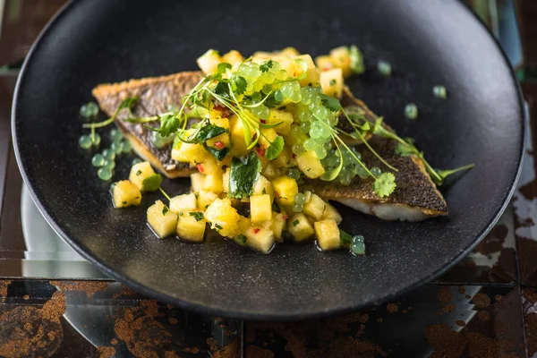 Grilled fish fillet with mango salsa served on black plate on brown tiled surface