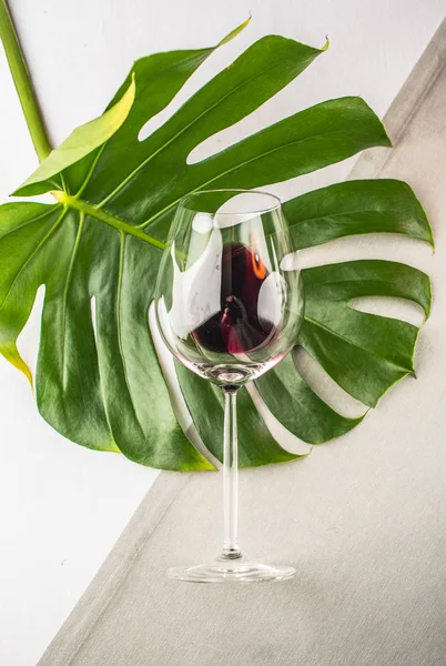 glass of red wine on green palm leaf on white surface