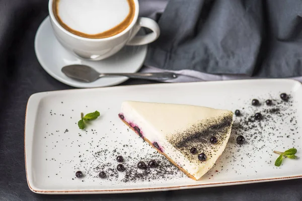 Berry cheesecake beyaz plaka üzerinde parça fincan kapuçino üzerinde gri masa örtüsü ile 