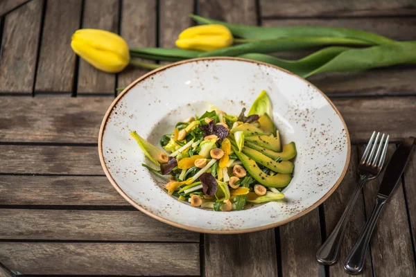 Fresh salad with with avocado and nuts in plate on wooden table with fresh tulips
