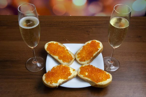 Two glasses of champagne (sparkling wine) and red caviar sandwiches