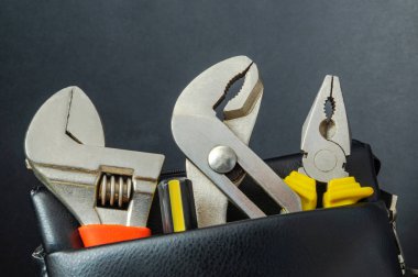 Siyah arka planda bir deri torbada araçlar-anahtarlar ve penye.