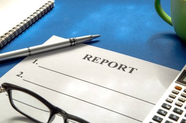 Mavi masada kalem, kahve, gözlük ve hesap makinesi ile rapor.