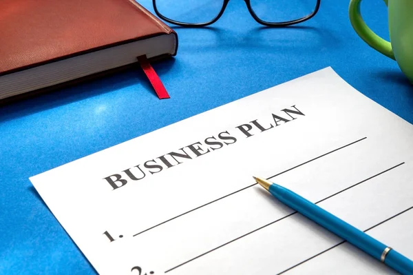 Una plantilla de plan de negocios para rellenar con bolígrafo, café, vasos y sobre mesa azul . — Foto de Stock