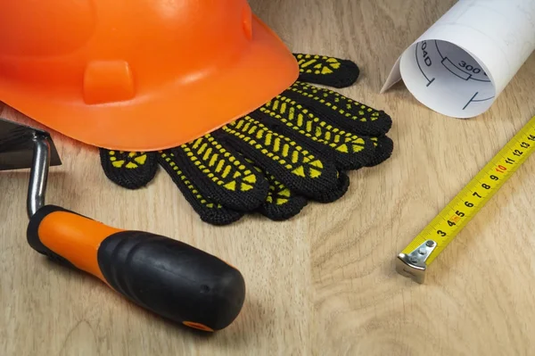 Protective helmet, gloves and tape measure on a wooden table.