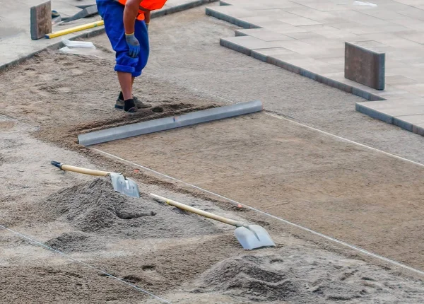 The worker evenly distributes crushed stone the tool.