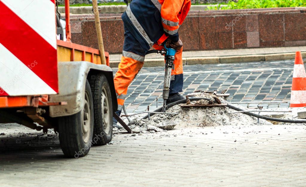 Male worker with full safety equipments drilling and repairing concrete driveway surface with jackhammer.