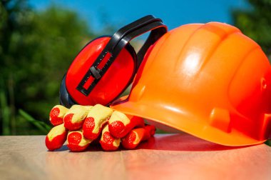 Koruyucu kask, kulaklıklar, ahşap bir masada eldiven, doğanın arka planına karşı.