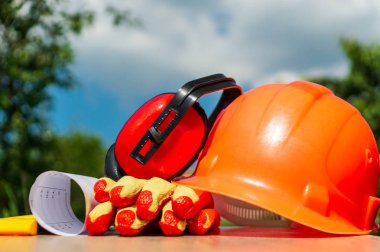 Koruyucu kask, kulaklıklar, ahşap bir masada eldiven, doğanın arka planına karşı.