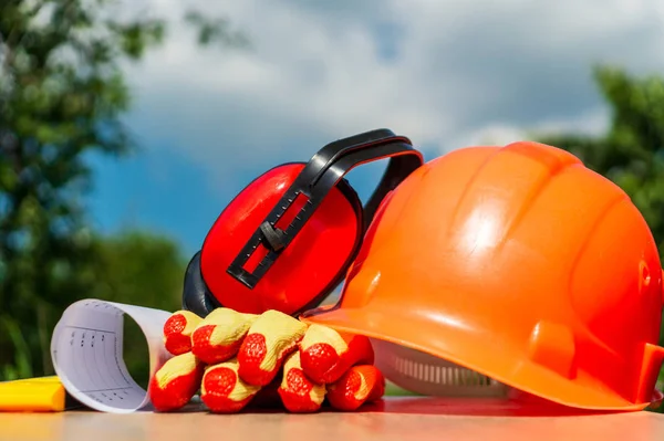Koruyucu kask, kulaklıklar, ahşap bir masada eldiven, doğanın arka planına karşı.