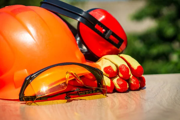 Capacete de proteção, fones de ouvido, luvas, óculos em uma mesa de madeira, contra o fundo da natureza . — Fotografia de Stock