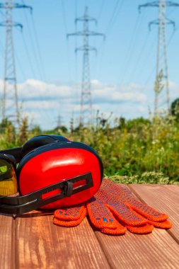 Headphones, gloves on a wooden table, against the background of nature and high voltage posts..