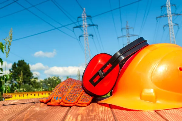Protective helmet, headphones, gloves on a wooden table, against the background of nature and high voltage posts..