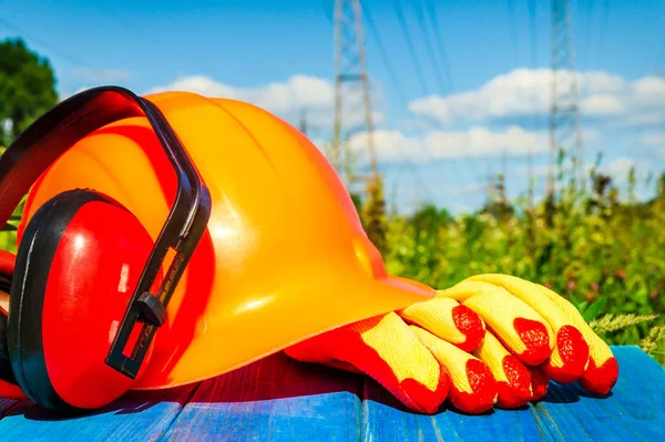 Protective helmet, headphones, gloves on a wooden table, against the background of nature and high voltage posts..