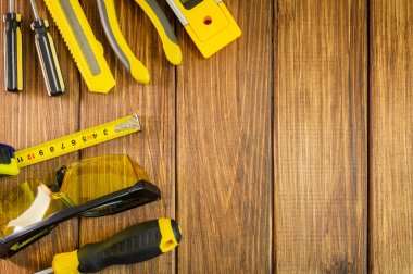 Ahşap arka planda eldiven, gözlük, inşaat seviyesi ve rulet, fotokopi alanı.