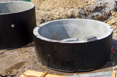 Şantiyede zemine beton kanalizasyon kuyularının montajı. Fosseptik tankları, taşma foseptik tankları için betonarme halkaların kullanımı.