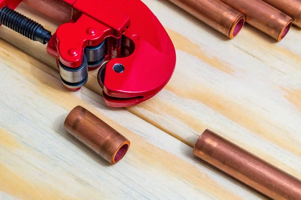 Red pipe cutter and copper pipes with connectors for plumbing repairs on wooden boards close up