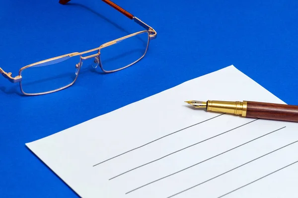 Blank for writing document with pen and glasses on a blue office desk