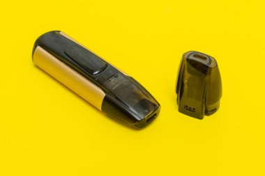 Sigara içmek için elektronik sigara ve sarı arka planda yedek şarjör.
