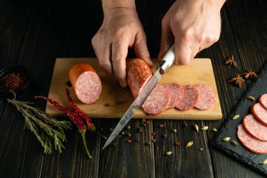 Şef bir restoranda öğle yemeği için sofra hazırlamak için et sosisini bıçakla keser. Hanın mutfağında ya da meyhanede atıştırmalık hazırlama kavramı.